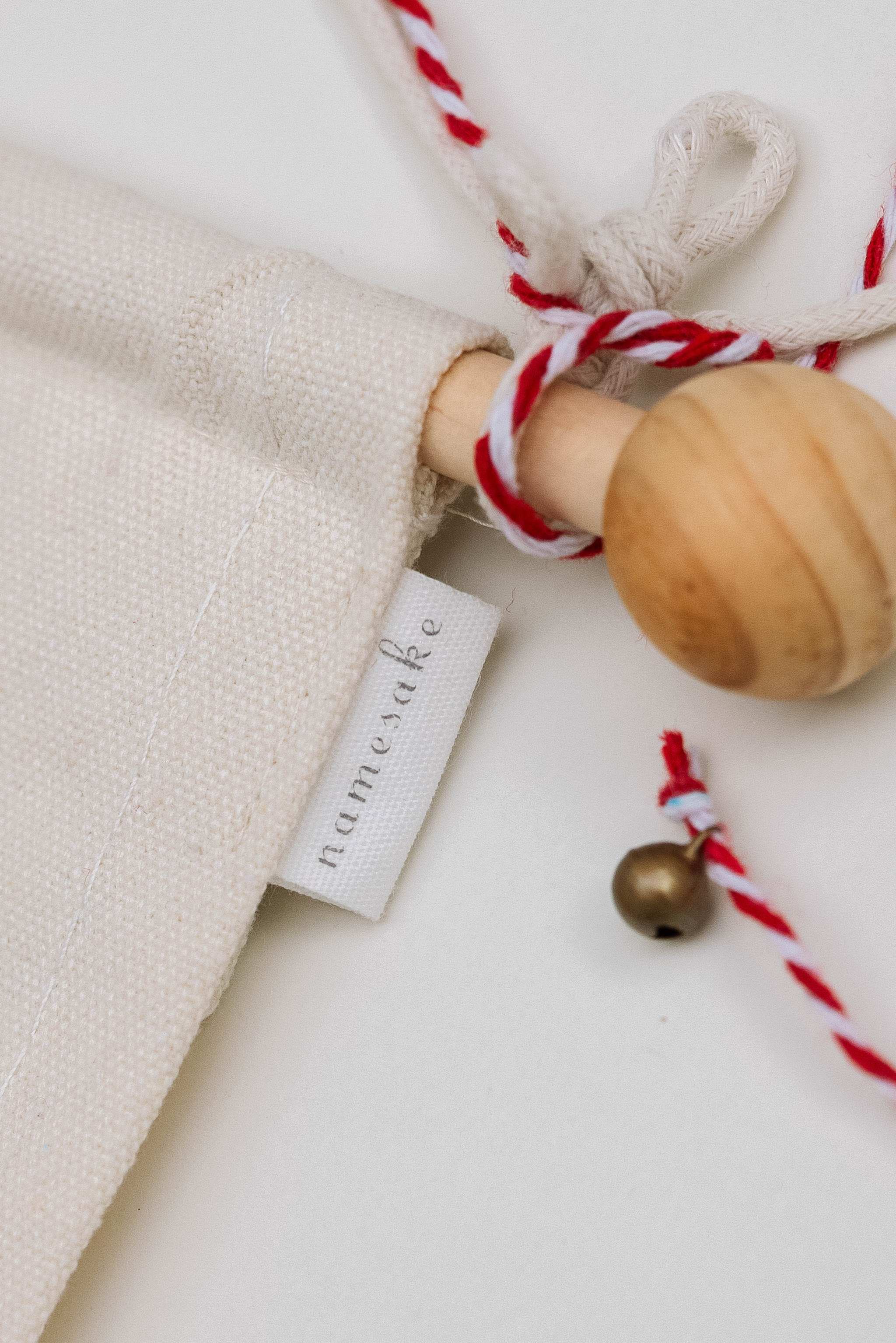 Close-up of embroidered advent calendar with wooden dowel, ivory cotton canvas, and red and white hanging string with tiny bell.