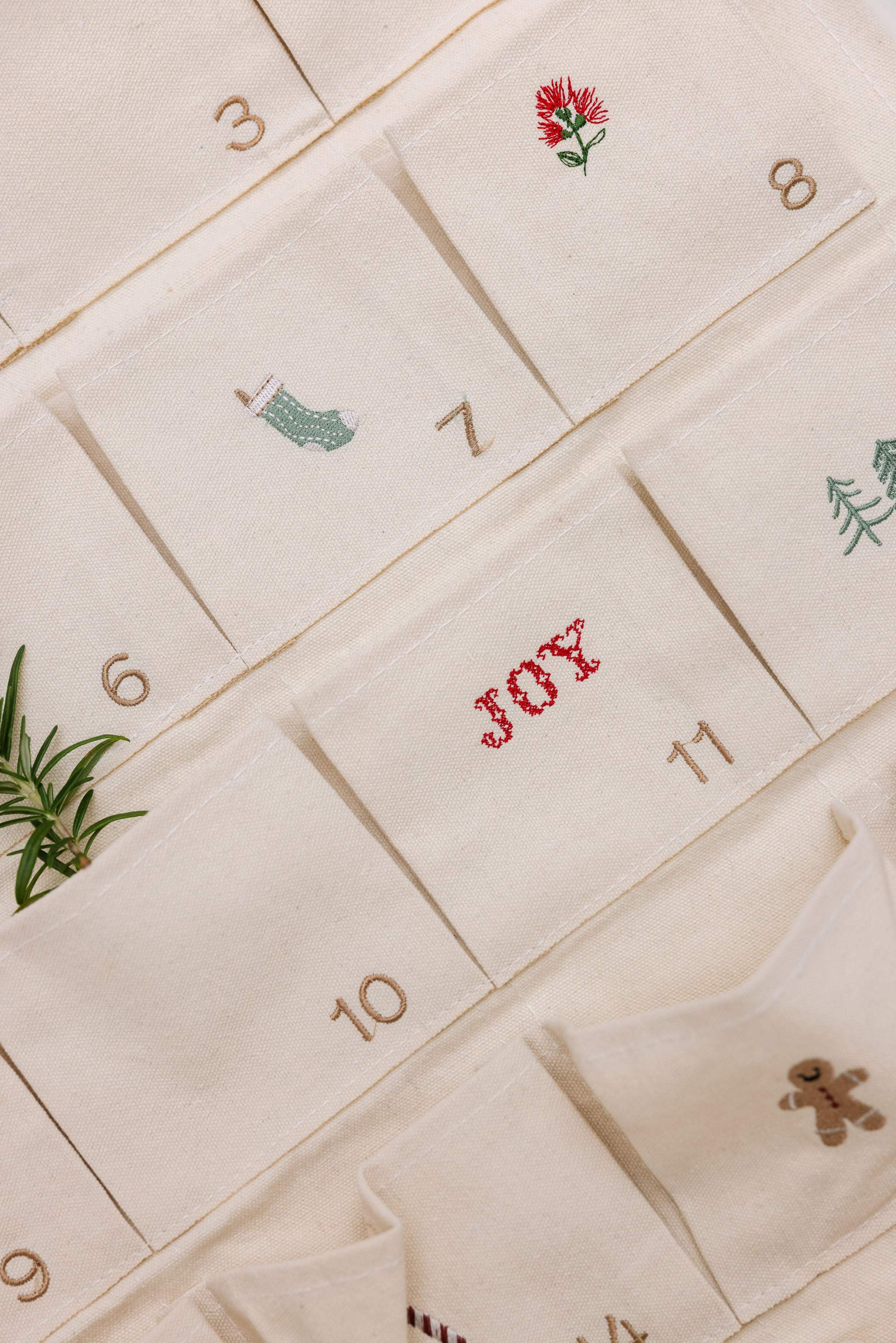 Embroidered Advent Calendar on ivory cotton canvas with festive designs and personalized text pockets.
