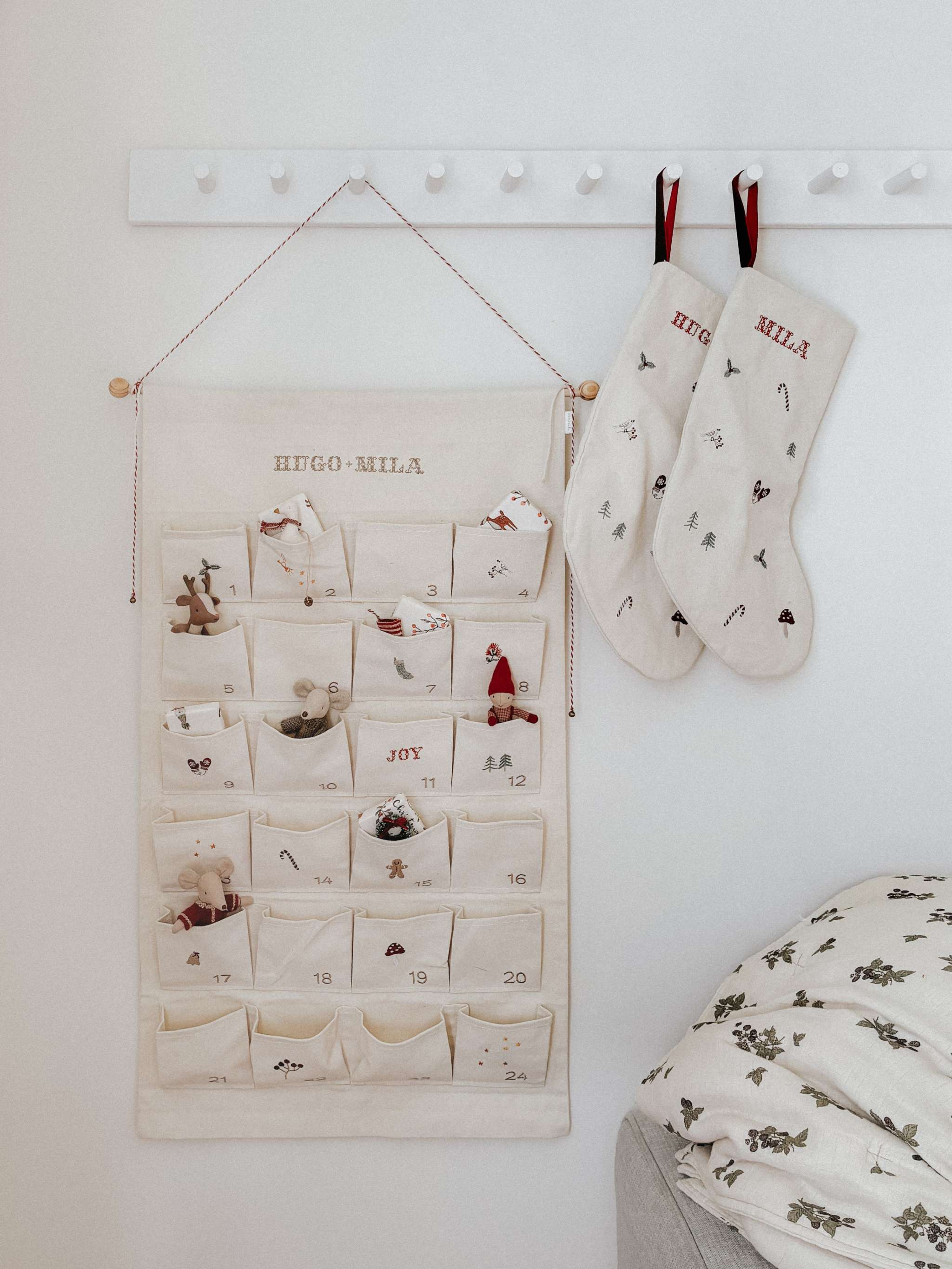 Embroidered Advent Calendar with personalized names, ivory cotton canvas, decorative pockets, and hanging string with tiny bells.