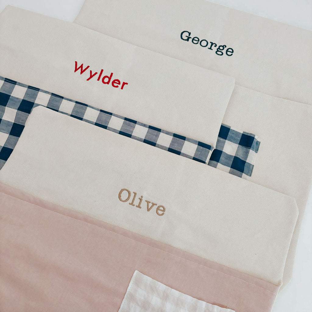 Personalised chair bags with various names embroidered in vintage pink and blue gingham designs.