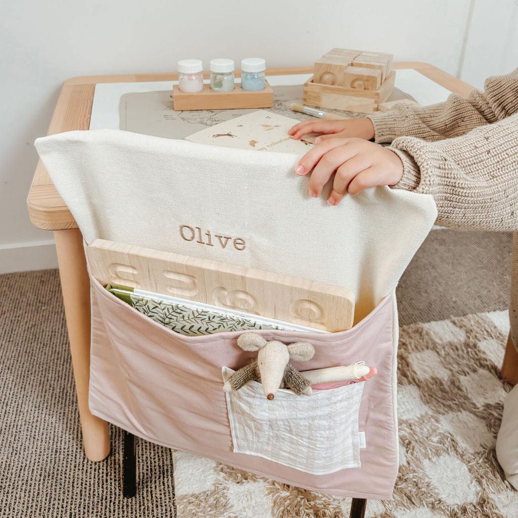 Vintage pink personalised chair bag on kids' chair, embroidered with "Olive," fits snugly for organized study environment, shown with books and toy.
