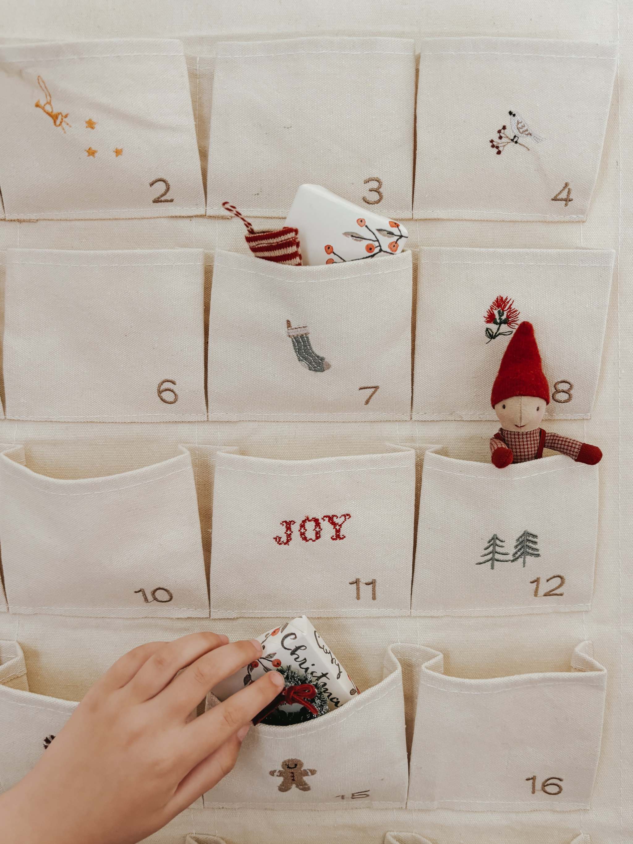 Embroidered Advent Calendar made of ivory cotton canvas with numbered pockets, whimsical embroidery, tiny bells, and personalized options.