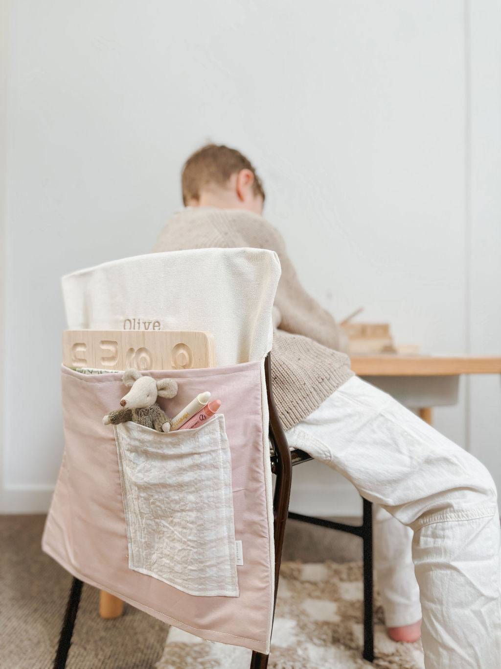 Child sitting with a personalised pink chair bag, ideal for organizing school supplies, made from durable cotton canvas.