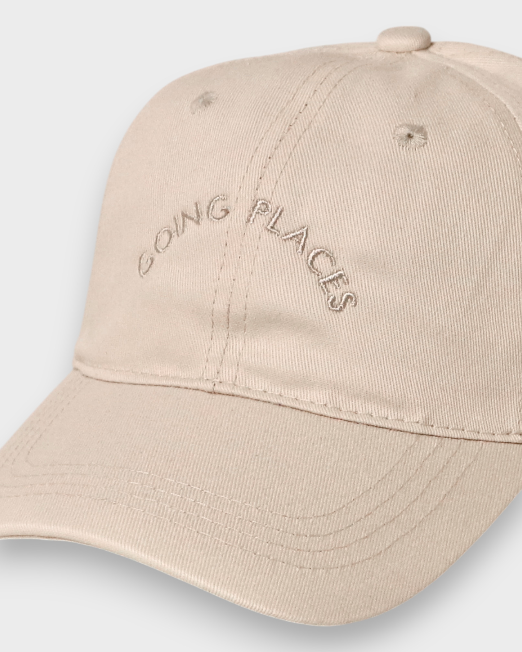 Personalised baseball cap with embroidered "Going Places" text on beige cotton.