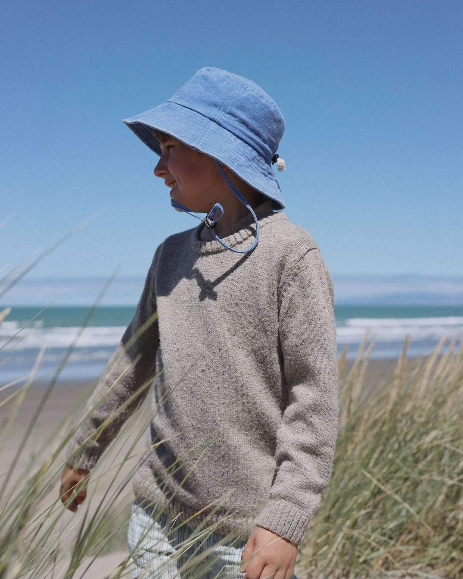Embroidered blue bucket hat on child at the beach, designed for ages 2-6, made in New Zealand.