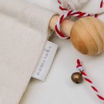 Close-up of embroidered advent calendar with wooden dowel, ivory cotton canvas, and red and white hanging string with tiny bell.