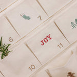 Embroidered Advent Calendar on ivory cotton canvas with festive designs and personalized text pockets.