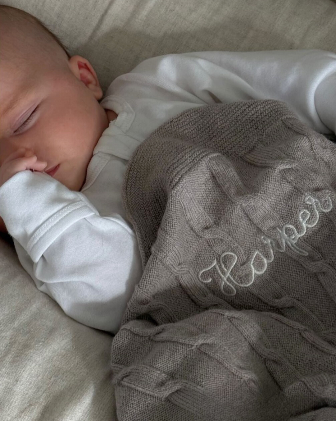 Baby sleeping peacefully wrapped in soft grey merino baby blanket embroidered with name
