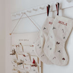 Linen stocking with holiday pattern and personalized names hanging on white hooks