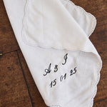 White ladies handkerchief with scalloped edge and custom black embroidery on wooden surface