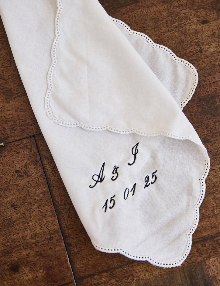White ladies handkerchief with scalloped edge and custom black embroidery on wooden surface