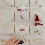 Embroidered Advent Calendar made of ivory cotton canvas with numbered pockets, whimsical embroidery, tiny bells, and personalized options.