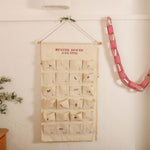 Embroidered ivory cotton canvas advent calendar with personalized Nordic Cross Stitch design and decorative red and white hanging string with tiny bells