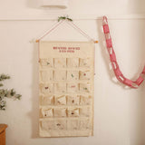 Embroidered ivory cotton canvas advent calendar with personalized Nordic Cross Stitch design and decorative red and white hanging string with tiny bells