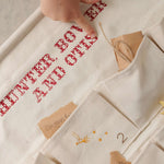Handcrafted ivory cotton canvas embroidered advent calendar with whimsical designs and personalized vintage-style red cross stitch text and pockets.