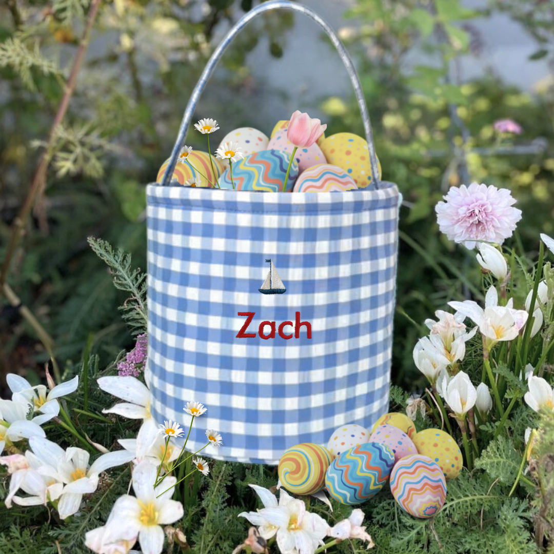 Personalised Easter Bucket with sailboat design and gingham pattern, holding colorful Easter eggs, surrounded by flowers.