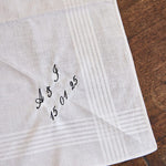 Personalized men's white cotton handkerchief embroidered with initials and date on wooden surface