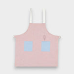 Kids pink linen apron with blue contrasting pockets and adjustable straps, suitable for ages 2-6.