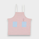 Kids pink linen apron with blue contrasting pockets and adjustable straps, suitable for ages 2-6.
